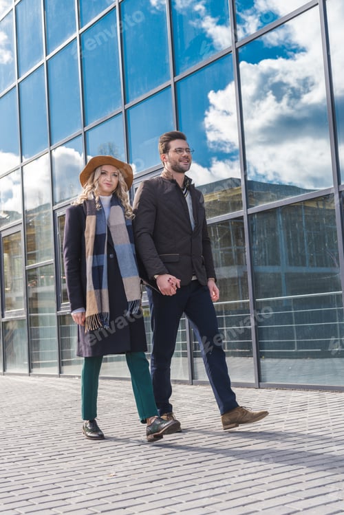 Preview: happy young couple in stylish autumn outfit walking together on street