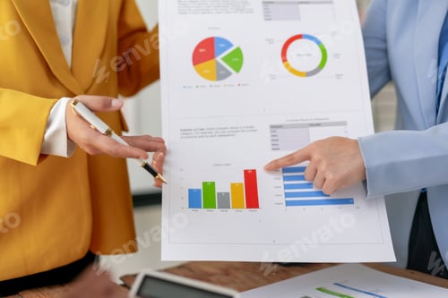 Preview: Business professionals analyzing colorful charts and graphs on paper during a meeting.