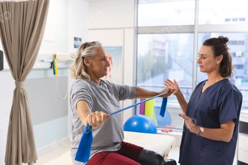 Preview: Caucasian female physiotherapist and senior woman with artificial leg using exercise band stretching
