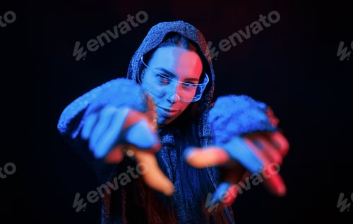 Preview: Does gestures by hands. Portrait of young girl that is in eyeglasses in blue neon lighting