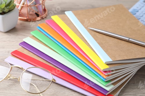Preview: Different copybooks, pen and glasses on wooden table, closeup