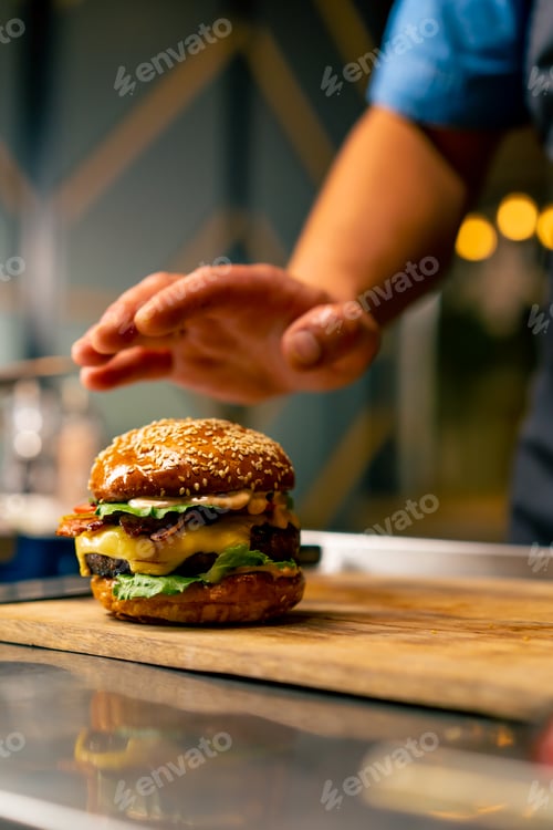 Preview: Close-up of a chef pinning a burger with beef patty with vegetables and cheese cooked in the kitchen