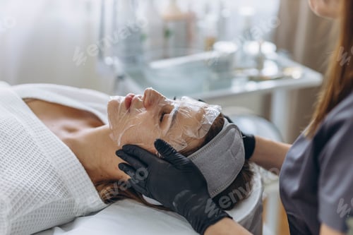 Preview: Cosmetologist cleanses young woman's face using professional skincare products.