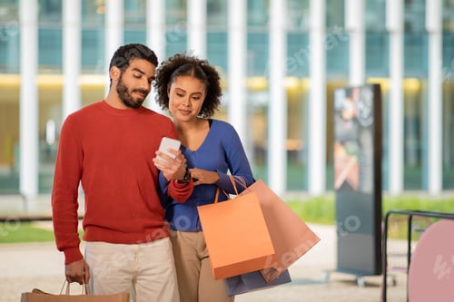 Preview: Happy Multicultural Couple Doing Shopping Using Cellphone Standing Outside