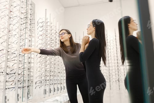 Preview: Optometrist helping woman choosing glasses in optics store