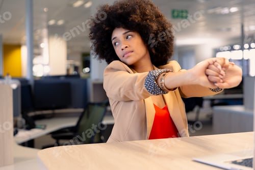 Preview: Tired young african american businesswoman with afro hairstyle stretching hands at workplace