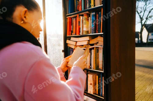 Preview: Young caucasian woman choosing books at free open public library at city park for book sharing