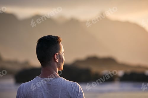 Preview: Portrait of pensive man on beach aganinst cliff at golden sunset. Tenerife, Canary Islands, Spain.