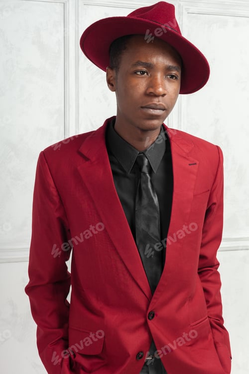 Preview: Young man poses in a red suit and hat in a simple indoor setting