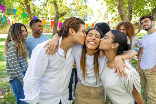 Preview: A woman smiles brightly as two friends kiss her on the cheeks during an outdoor gathering