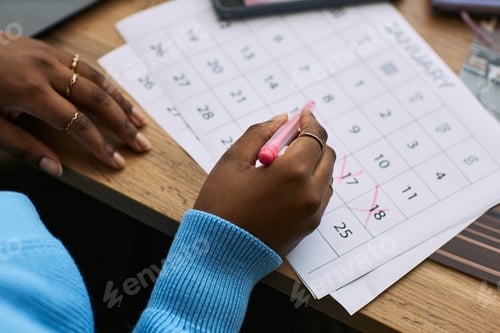 Preview: Young Black Woman Marking Menstrual Cycle Dates on Calendar at Desk