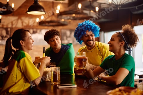 Preview: Group of happy sports fans celebrating and toasting with beer in a bar.