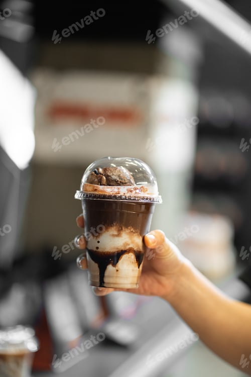 Preview: hand of woman holding a take-out iced affogato chocolate at coffee shop.