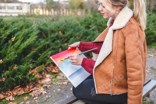 Preview: Side view of the painter sitting on a bench and paints a picture
