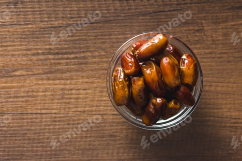 Preview: Dried dates fruit in bowl on wooden table. Top view.