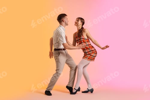 Preview: Happy couple in retro outfits dancing on color background