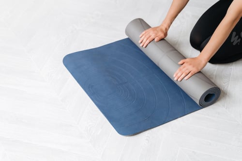 Preview: Woman rolling up blue yoga mat on floor