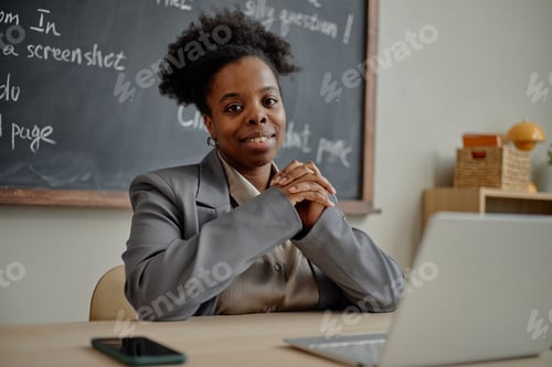 Preview: Portrait of Young Adult Black Woman Smiling While Sitting at Desk in Classroom