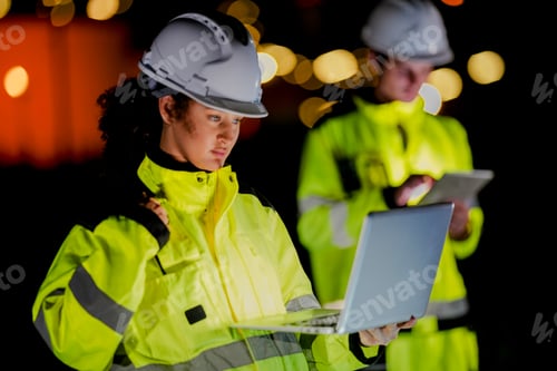 Preview: engineers in reflective safety gear review plans on a tablet during a night shift.
