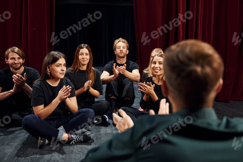 Preview: Sitting on the floor. Group of actors in dark colored clothes on rehearsal in the theater