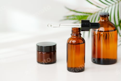 Preview: Collection of Amber Glass Bottles and Jars for Essential Oils on a White Surface