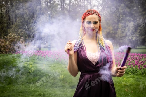 Preview: A girl with a smile with bright makeup and colored braids in a purple dress blows artificial purple