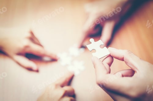 Preview: High Angle View Of Businesspeople Hand Solving Jigsaw Puzzle On Wooden Desk