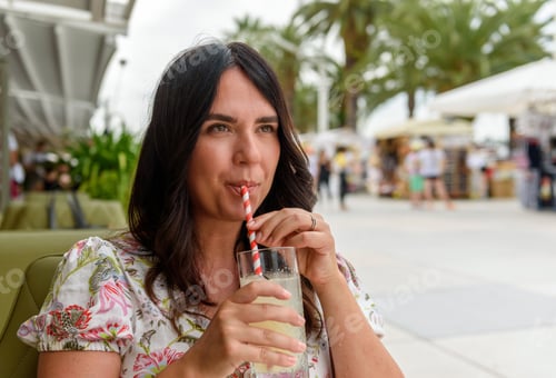 Preview: Pretty girl with long hair sitting in bar outdoor in city, drinking lemonade on straw