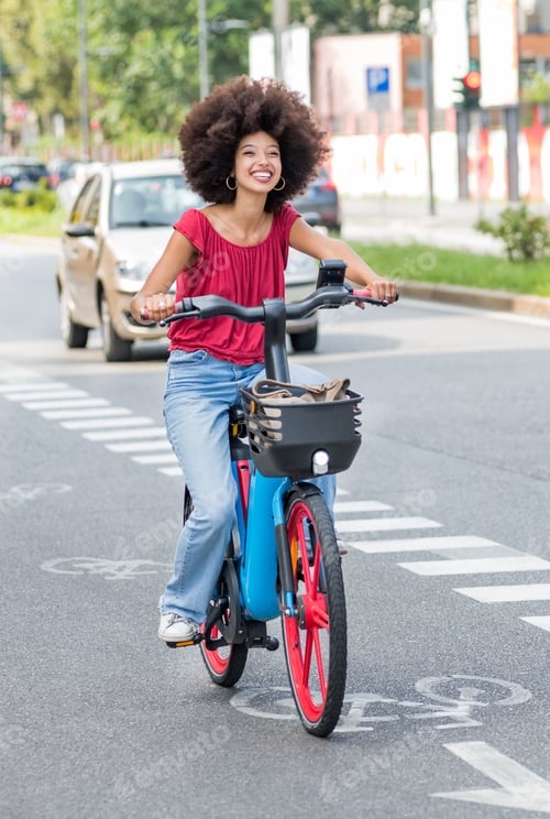 Preview: Smiling young ethnic woman riding electric bicycle on asphalt road in daylight