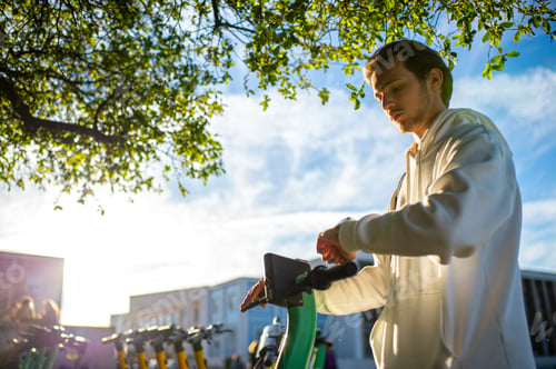 Preview: Student looking at his smartwatch while holding onto an electric scooter. Man checks time