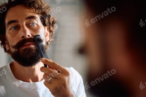 Preview: Mature man combing beard in front of a mirror in the bathroom.