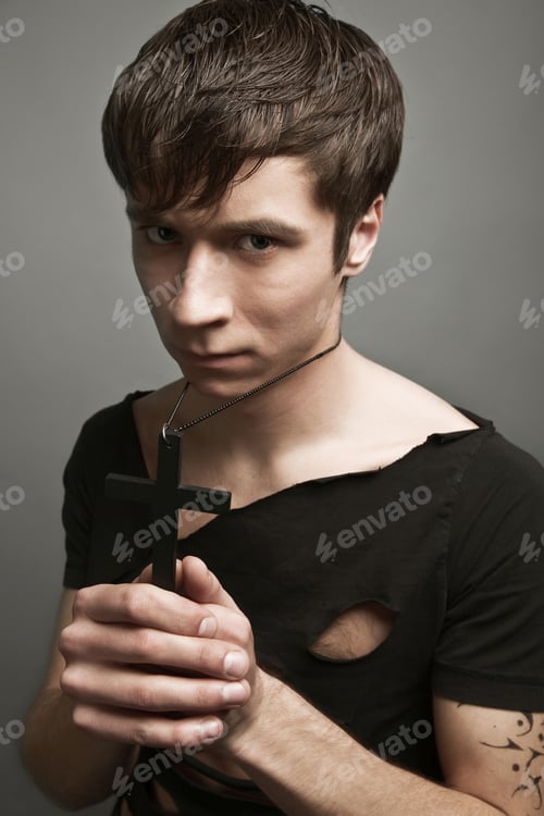 Preview: Young man in modern black clothing holding big black cross in hands