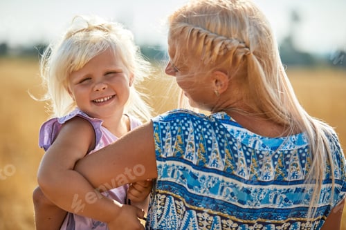 Preview: happy mother holding baby smiling on a wheat field in sunlight