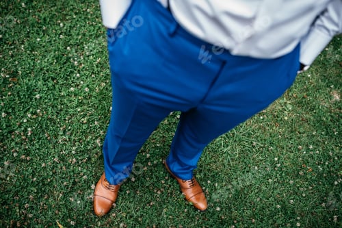 Preview: Stylish young man stands in lush green grass in a blue trousers