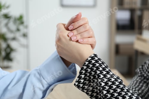 Preview: Businesswomen arm wrestling at table in office, closeup