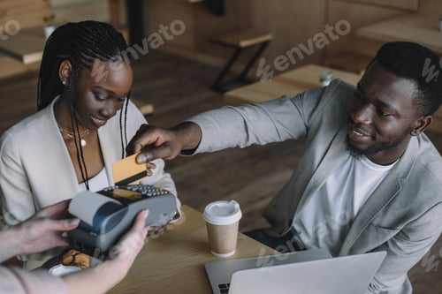 Preview: african american man paying for order with credit card while spending time with friend in cafe