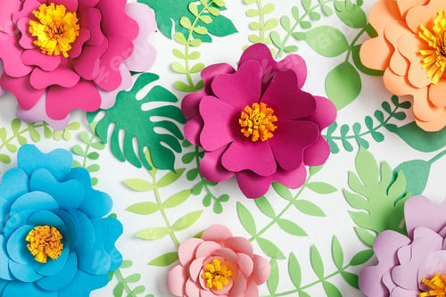 Preview: top view of pink, purple, orange, blue paper flowers and green leaves on white background