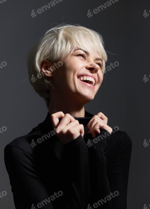 Preview: Joyful young woman with short blonde hair smiling brightly against a dark background, embodying