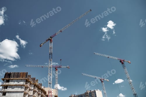 Preview: Construction cranes work on creation site against blue sky background