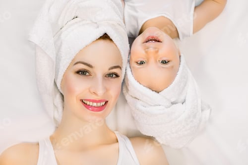 Preview: Smiling mother and daughter lying on white background, bathtime concept. Pretty young woman with