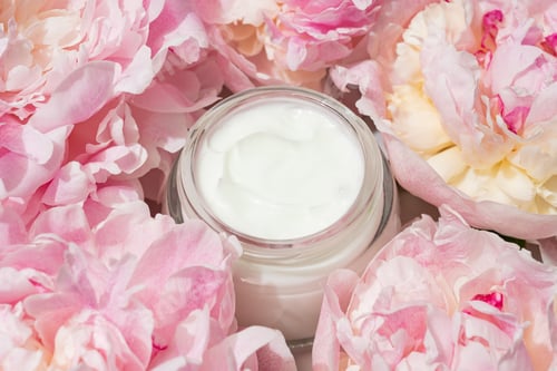 Preview: Open cream jar with pink peonies on soft backdrop. Fresh, floral beauty flat lay for skincare