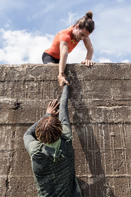 Preview: Young male free climber at top of sea wall helping friend climb up