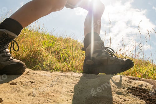 Preview: woman walking with hiking boots on rock against sunny background