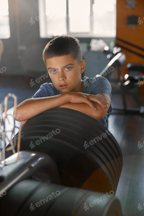 Preview: Portrait of teenage boy posing for camera over sport club weightlift equipment