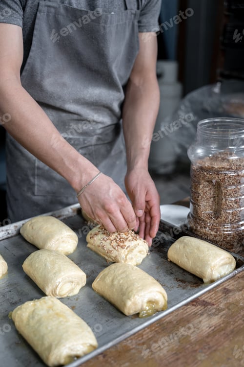 Preview: A young Hispanic man is covering a pastry cream filled bun with sweet nut toppings