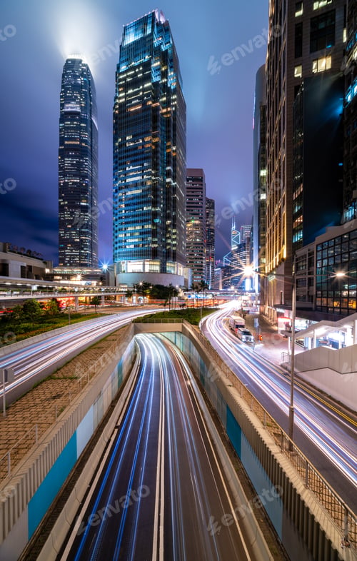 Preview: Skyscraper buildings and traffic on road with blurred cars light trails at night, Hong Kong, China