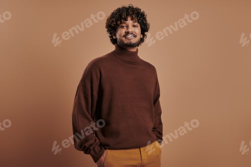 Preview: Handsome Indian man looking at camera and smiling against brown background