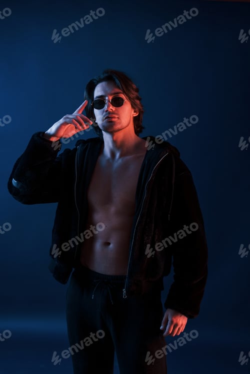 Preview: Beautiful man in glasses and black clothes is in the studio with blue neon lighting