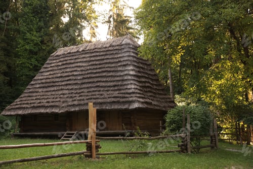 Preview: Old wooden hut with straw roof behind fence in forest
