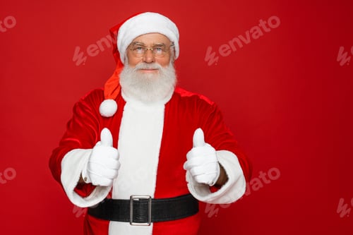 Preview: Santa Claus showing thumbs up hands like gesture looking at camera isolated red background.